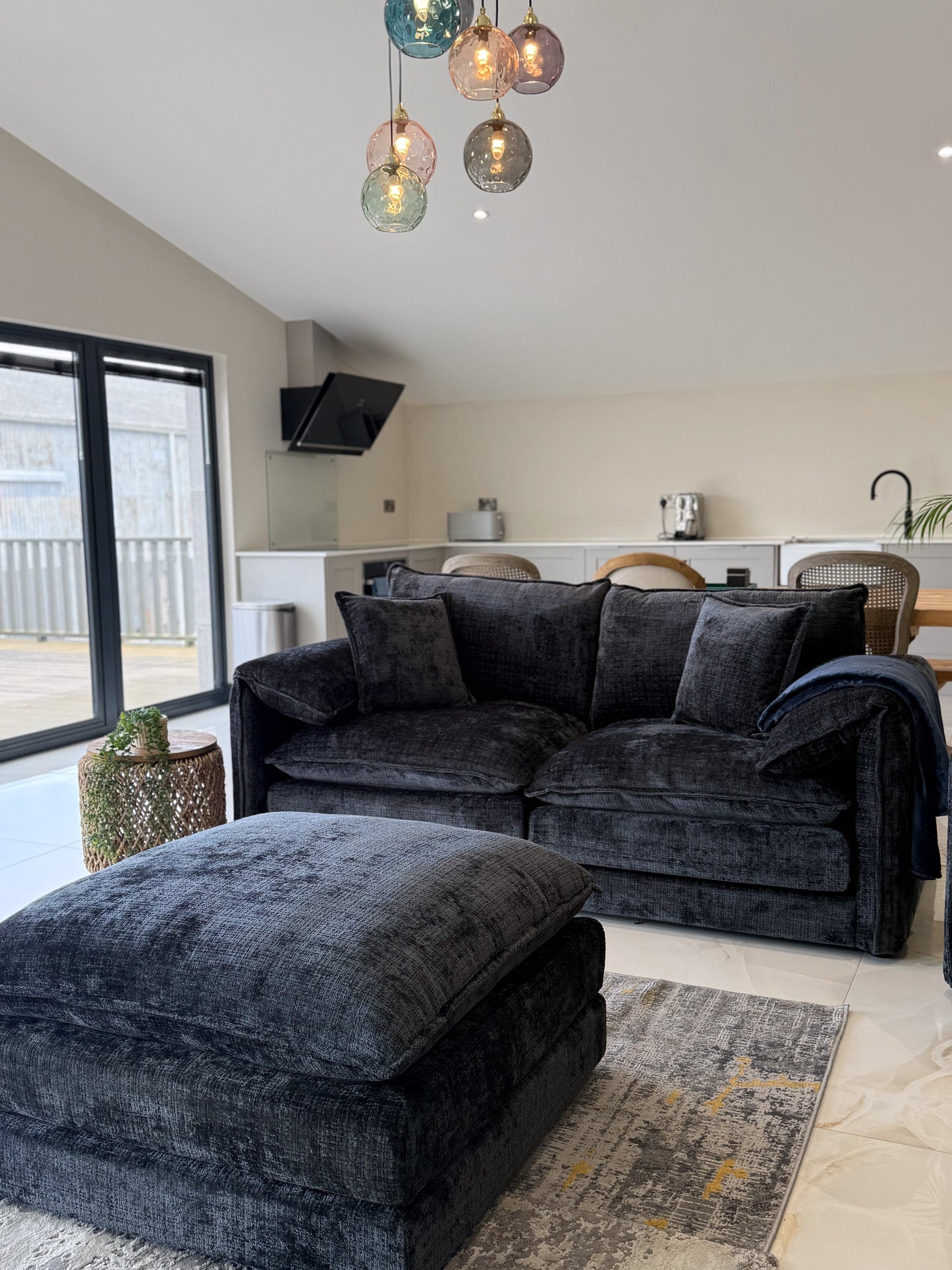 Modern living room with a Black sectional sofa, ottoman, and colorful pendant lights.