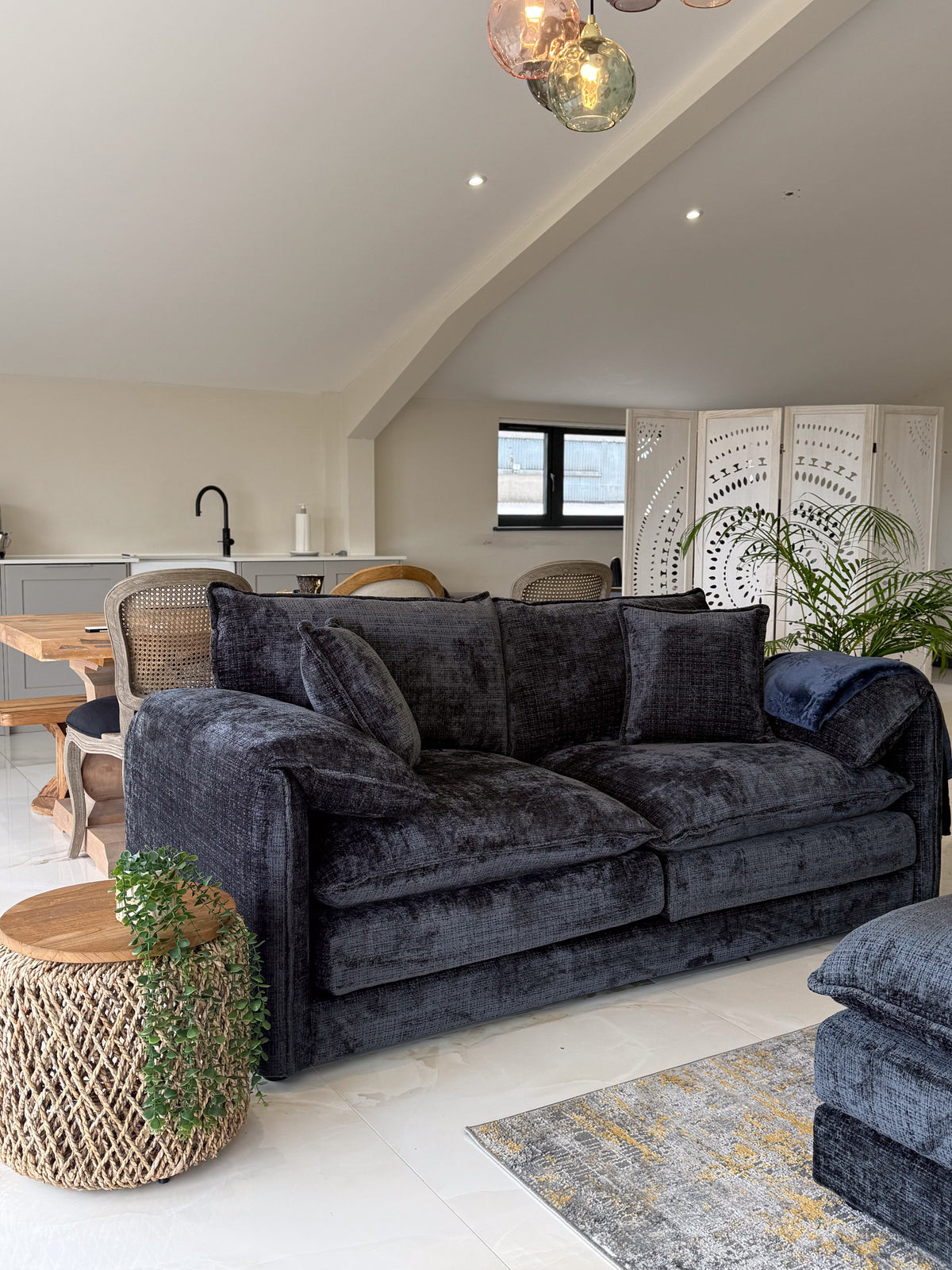 Black sofa in a living room with a kitchen in the background