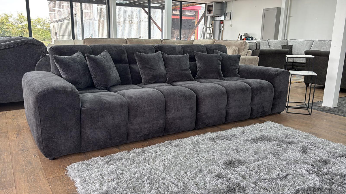 Large black sectional sofa in a living room setting with a rug and windows in the background.