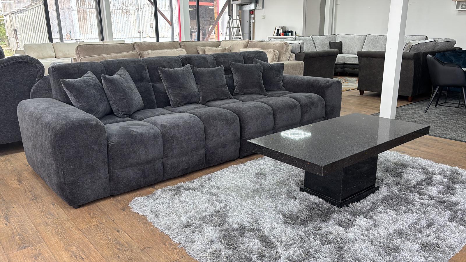 Black sectional sofa in a showroom setting with a coffee table in front.