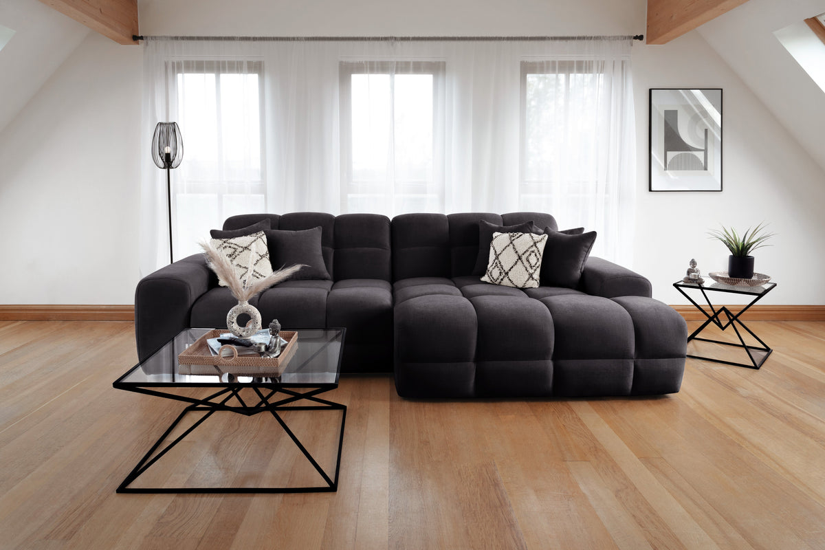 Modern living room with a large black sectional sofa, glass coffee table, and decorative items.