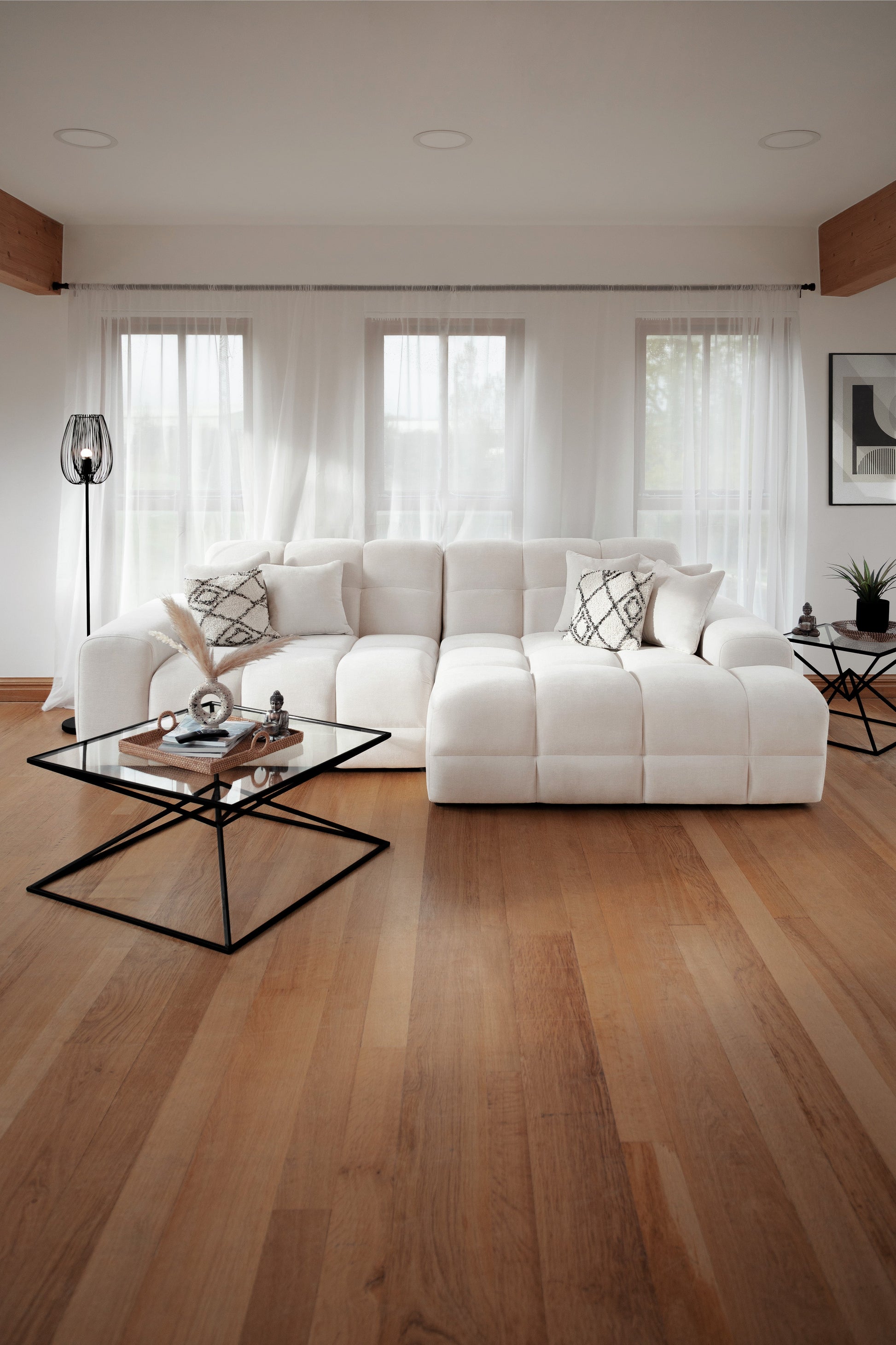 Modern living room with a white sectional sofa, glass coffee table, and wooden floor.