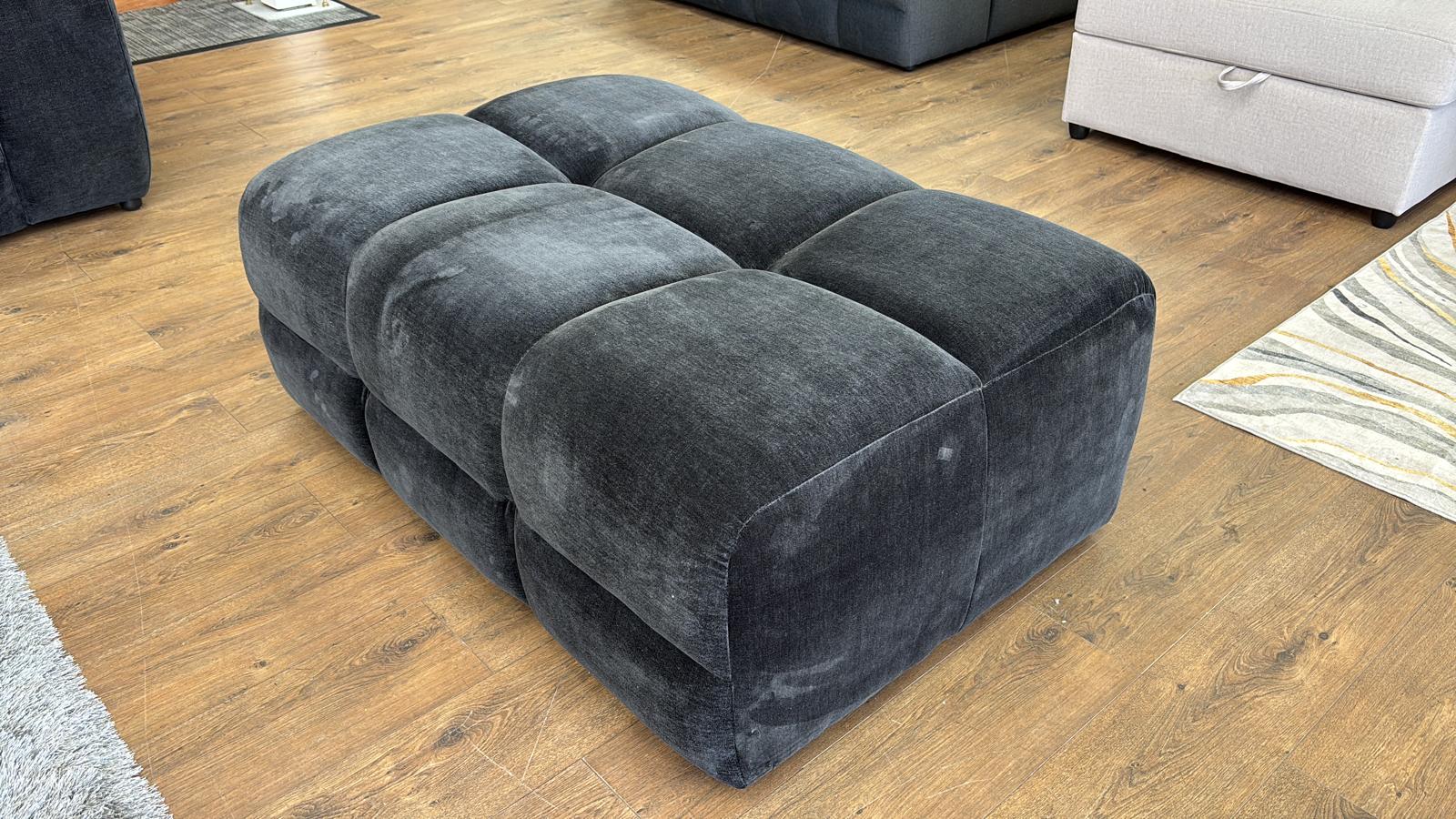 Black sectional sofa on a wooden floor with a rug and part of a couch visible.