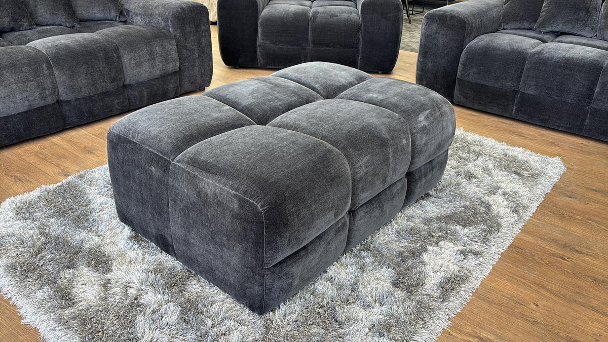 Black textured ottoman on a rug with matching gray sofas in the background
