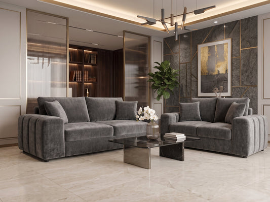 A modern living room featuring a dark gray velvet sectional sofa and a matching two-seater loveseat, styled with a glass-top coffee table, a potted plant, and contemporary wall decor.
