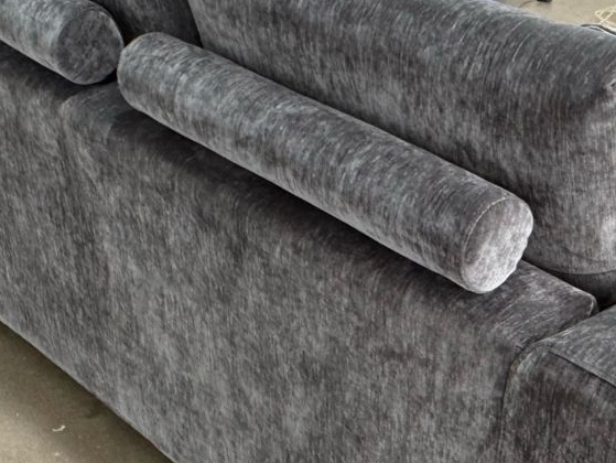 Close-up of a dark gray textured fabric sofa with cylindrical bolster armrests and matching back cushions.
