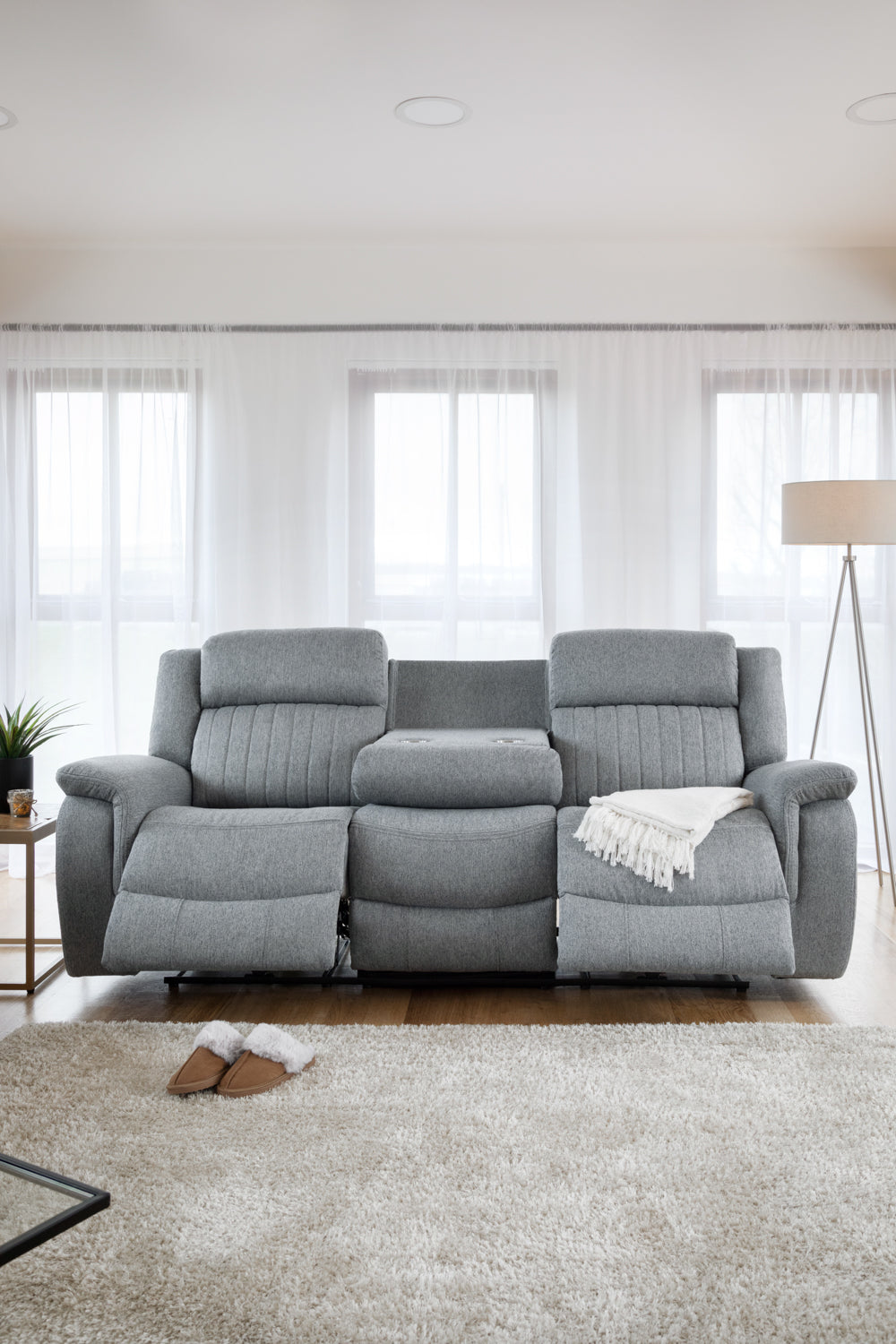 Gray sectional sofa in a living room with large windows and a lamp.