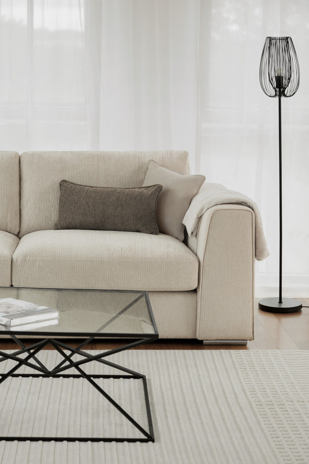 Beige sofa with a glass coffee table and black floor lamp in a living room setting.