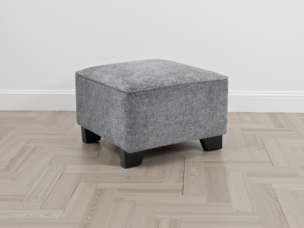 Gray upholstered ottoman on a wooden floor with a white wall background