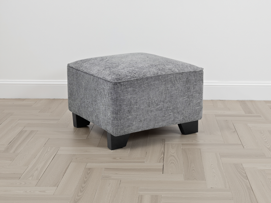 Gray upholstered ottoman on a wooden floor with a white wall background