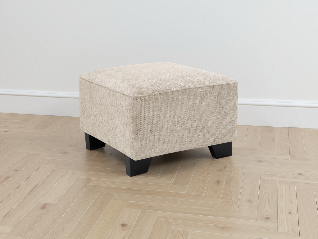 Beige ottoman with black legs on a wooden floor against a white wall