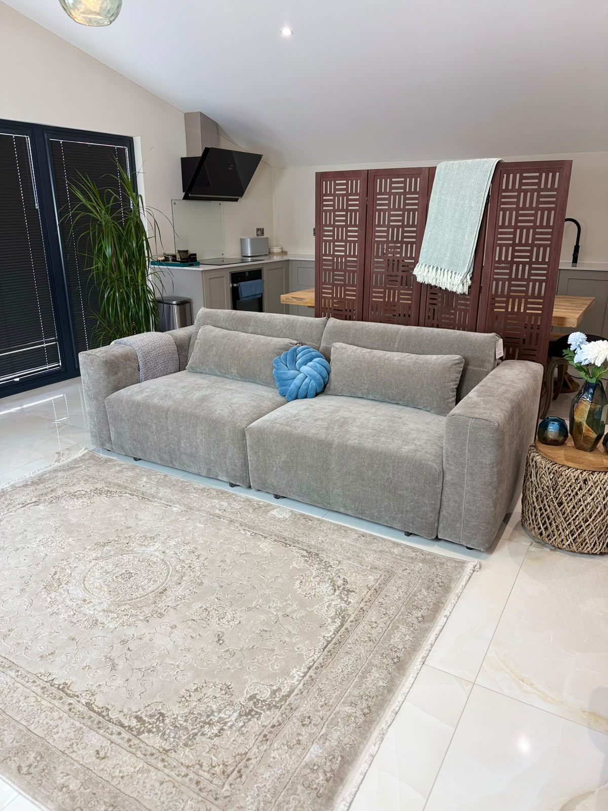 A modern light gray fabric sectional sofa with a round blue decorative pillow, set on a large beige patterned area rug in a bright, contemporary living room.