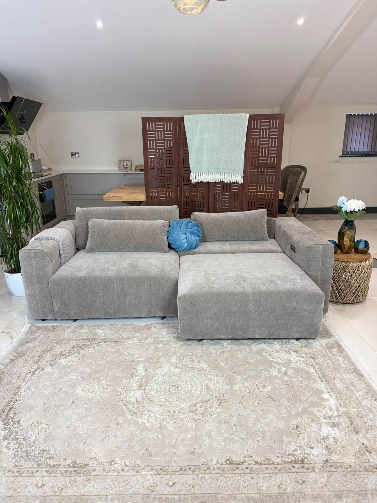 A light gray modular fabric sofa with a chaise lounge, styled in a home interior with a beige patterned area rug, a blue decorative pillow, and a wooden screen in the background.