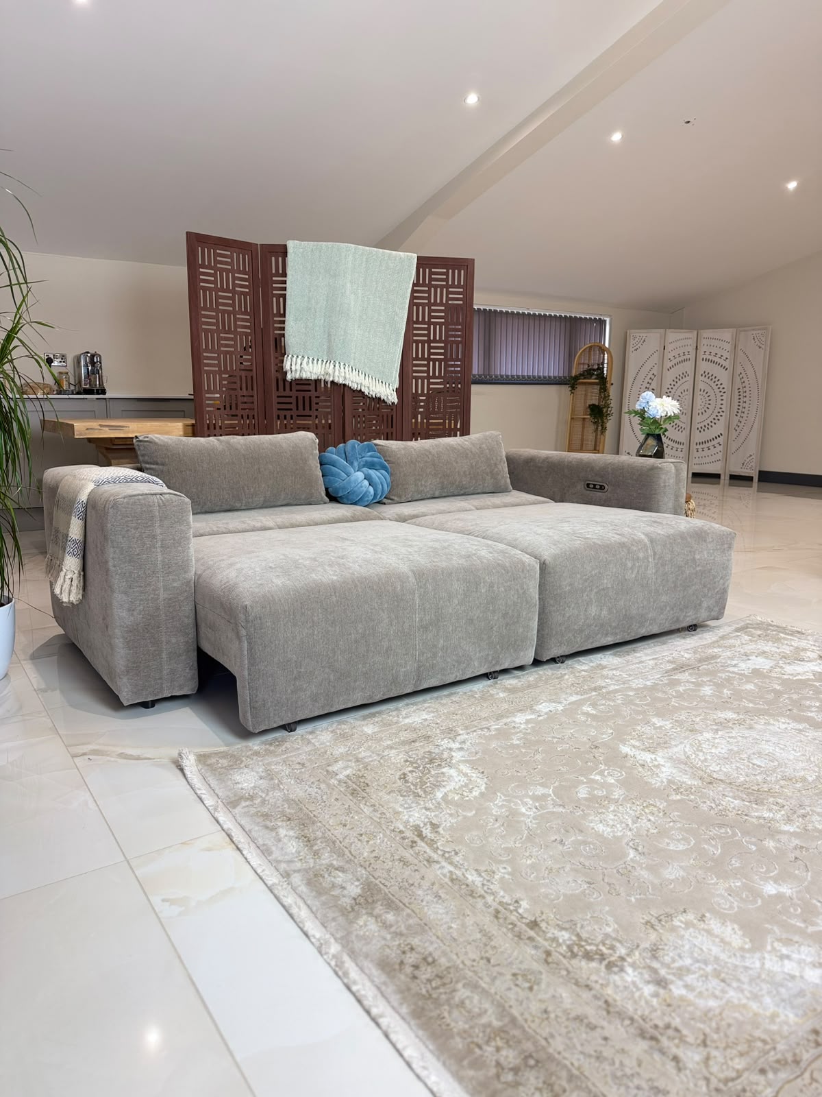 A modern modular sectional sofa in a light gray textured fabric, styled in a bright, contemporary living room with a beige patterned rug, a blue accent pillow, and decorative screens in the background.