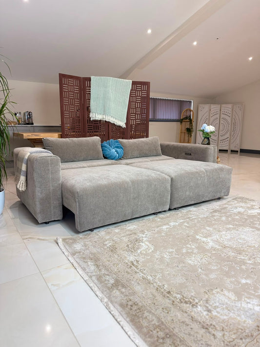 A modern modular sectional sofa in a light gray textured fabric, styled in a bright, contemporary living room with a beige patterned rug, a blue accent pillow, and decorative screens in the background.