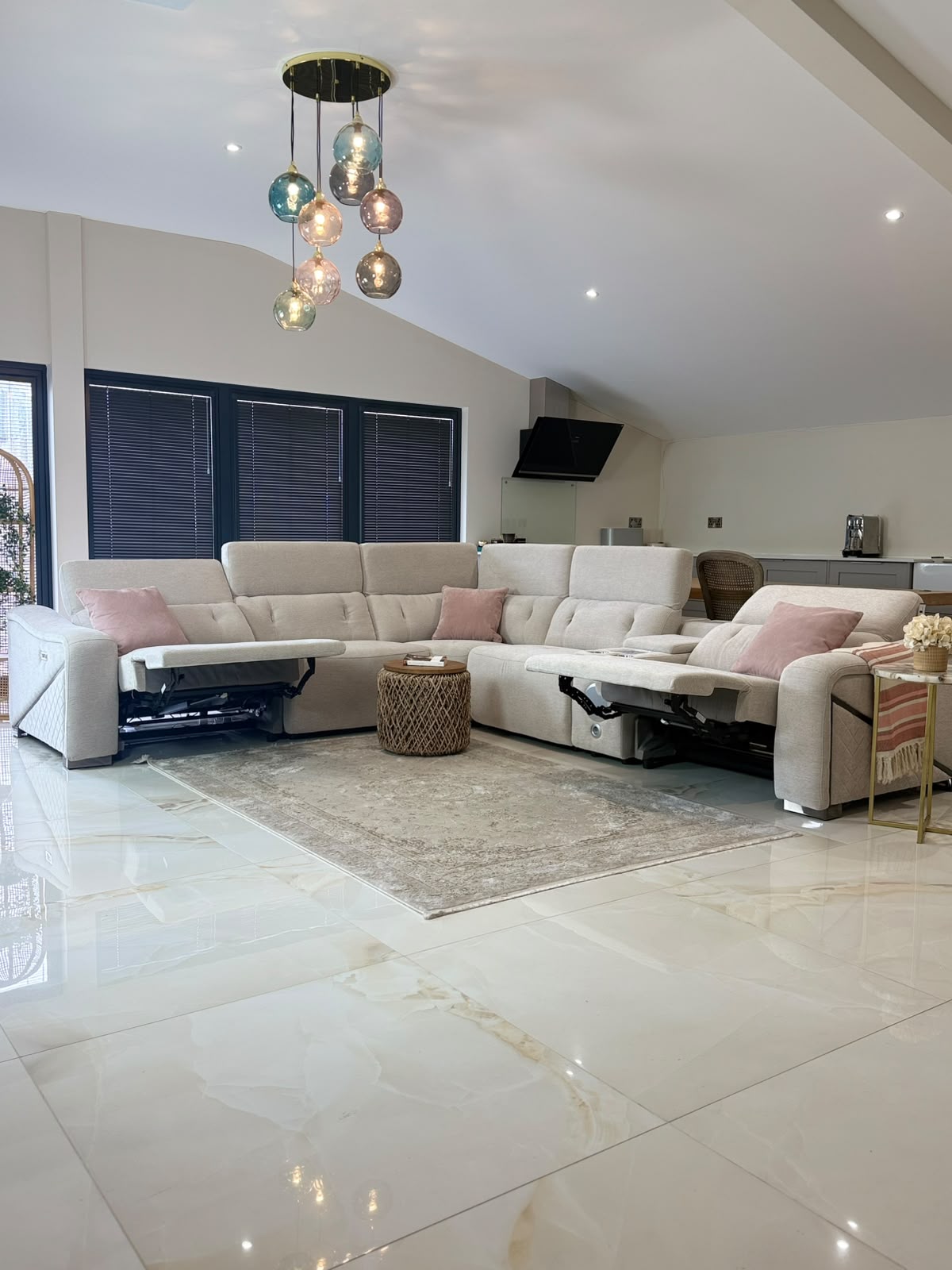 A large cream-colored modular sectional sofa with built-in media screens and power outlets, styled in a modern living room with a patterned area rug and a glass chandelier.