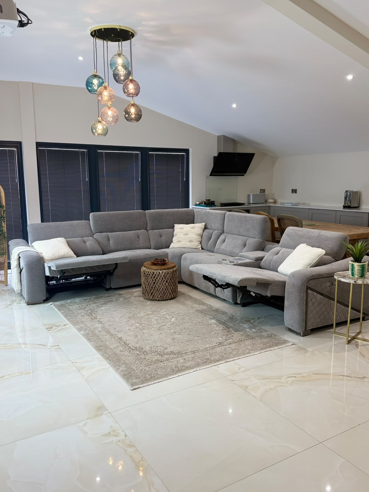 A large grey modular reclining sectional sofa in a modern open-plan living room with a slanted ceiling, marble tile floors, and a decorative area rug.
