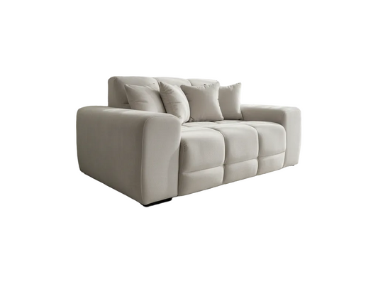 A modern three-seater sofa upholstered in a light beige fabric, featuring a low-profile rectangular silhouette, chunky armrests, and four matching throw pillows, shown against a plain white background.