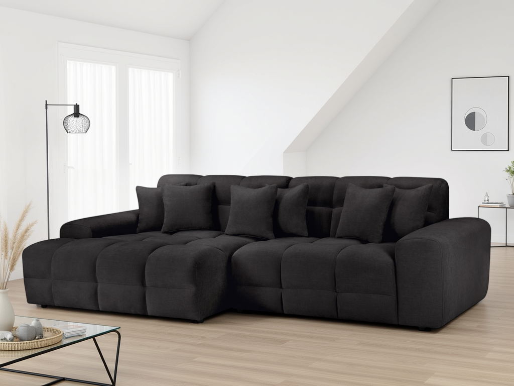 Black sectional sofa in a modern living room with a white wall and minimal decor.