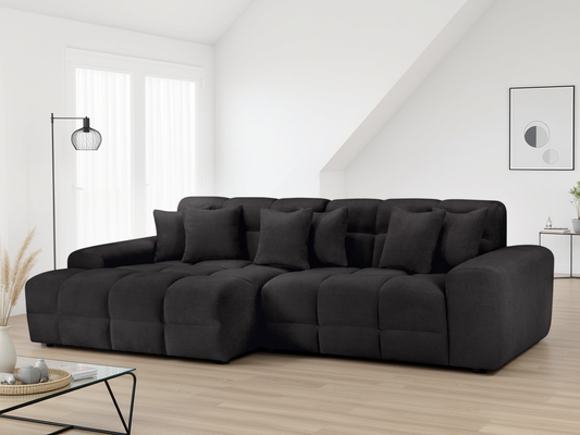 Black sectional sofa in a modern living room with a white wall and minimal decor.