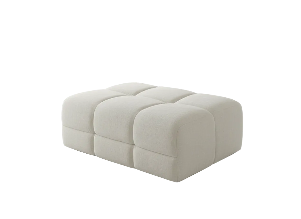 A modern tufted ottoman in a light cream or off-white fabric, shown from a three-quarters perspective on a solid white background.