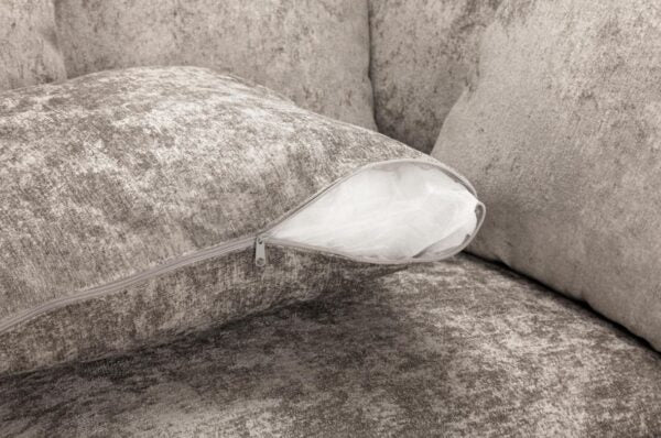 A close-up of a textured gray throw pillow with a zipper opening, showing a white inner insert, set against a matching gray upholstered sofa.